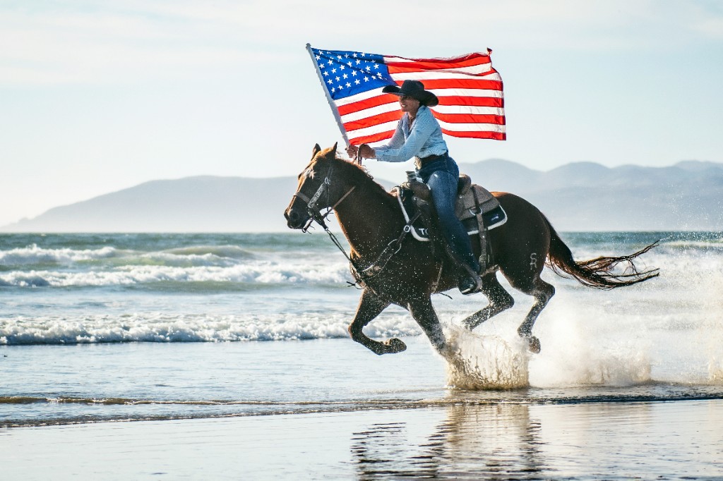 Rider carrying an American flag on horseback along the beach